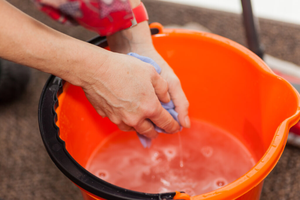 Two hands in a mop bucket ringing water from a sponge