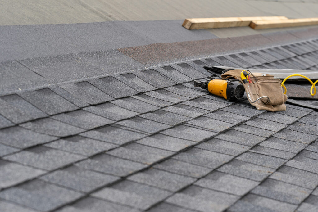 Toolbelt with instrument and nail gun lying on asphalt or bitumen shingle on top of the new roof under construction residential house or building