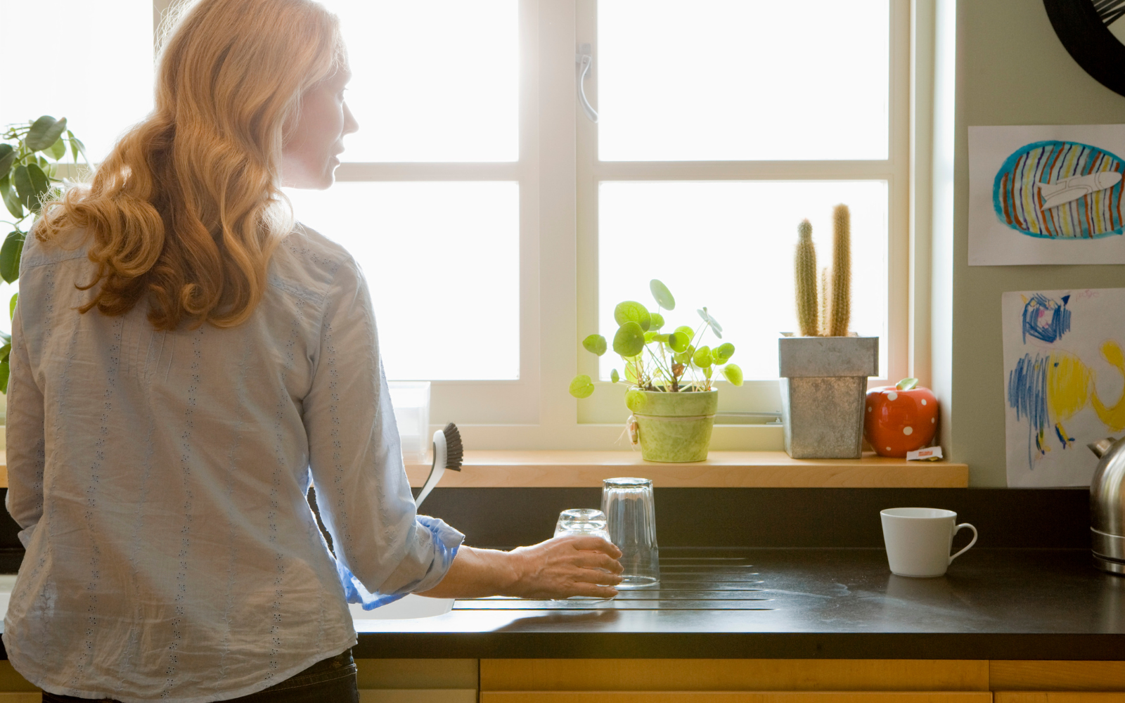 Women cleaning dishes in her kitchen looking out a casement window