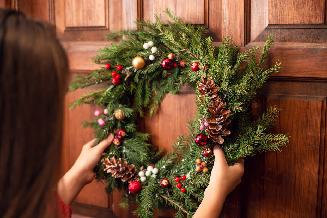 a woman placing a wreath on a door using a hook