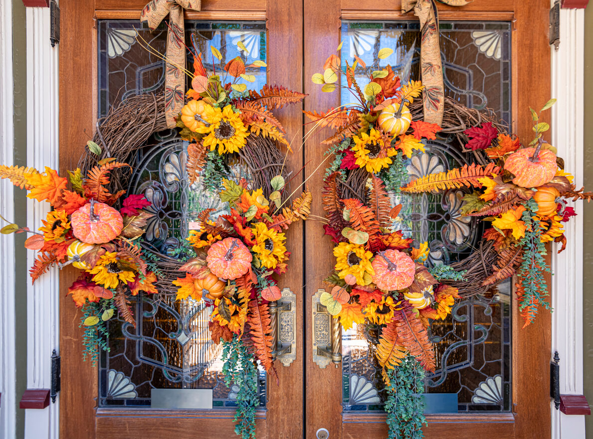 two fall-themed wreaths hung using ribbon next to each other on double doors.